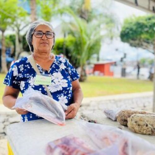 A 6ª edição da Feira Santa do Pescado começou movimentando a Praça Admar Braga Guimarães, a conhecida Praça dos Táxis, em Valença, nesta quinta-feira (26). Logo no primeiro dia, o espaço foi tomado pela diversidade de produtos locais, reunindo pescadores, artesãos e instituições. A iniciativa também contou com o apoio de diversas secretarias municipais, que contribuíram para uma programação ainda mais diversa. Entre os expositores, Dona Maria Pereira, conhecida como Cida do Marisco, apresentou produtos frescos e de qualidade, reforçando a tradição da pesca familiar. O público também pôde conhecer o universo do aquarismo com o stand da Betta Premium, representado por Ylan Leocadia e Lucas Paraíso, que expuseram peixes ornamentais e acessórios. No artesanato, Jacinete de Jesus, da marca Crochê da Jacy, apresentou peças como saias, camisas e vestidos, resultado de mais de cinco anos de dedicação ao artesanato. Já Cláudia Cardoso, com mais de 25 anos de experiência no crochê, destacou o ofício como fonte de “equilíbrio e saúde mental”. O Núcleo do Artesanato Territorial da Costa do Dendê, também esteve presente, com produtos confeccionados em sisal e juta, valorizando a produção regional. A diversidade também esteve presente no cultivo de plantas. Marle Pereira, que há cinco anos comercializa espécies cultivadas em seu próprio sítio, levou para a feira exemplares como rosas do deserto, orquídeas e antúrios vermelhos. Com orgulho, ela contou que a renda obtida com as vendas contribui para custear a faculdade de psicologia da filha.