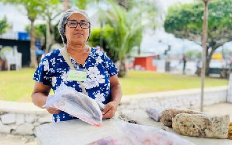 A 6ª edição da Feira Santa do Pescado começou movimentando a Praça Admar Braga Guimarães, a conhecida Praça dos Táxis, em Valença, nesta quinta-feira (26). Logo no primeiro dia, o espaço foi tomado pela diversidade de produtos locais, reunindo pescadores, artesãos e instituições. A iniciativa também contou com o apoio de diversas secretarias municipais, que contribuíram para uma programação ainda mais diversa. Entre os expositores, Dona Maria Pereira, conhecida como Cida do Marisco, apresentou produtos frescos e de qualidade, reforçando a tradição da pesca familiar. O público também pôde conhecer o universo do aquarismo com o stand da Betta Premium, representado por Ylan Leocadia e Lucas Paraíso, que expuseram peixes ornamentais e acessórios. No artesanato, Jacinete de Jesus, da marca Crochê da Jacy, apresentou peças como saias, camisas e vestidos, resultado de mais de cinco anos de dedicação ao artesanato. Já Cláudia Cardoso, com mais de 25 anos de experiência no crochê, destacou o ofício como fonte de “equilíbrio e saúde mental”. O Núcleo do Artesanato Territorial da Costa do Dendê, também esteve presente, com produtos confeccionados em sisal e juta, valorizando a produção regional. A diversidade também esteve presente no cultivo de plantas. Marle Pereira, que há cinco anos comercializa espécies cultivadas em seu próprio sítio, levou para a feira exemplares como rosas do deserto, orquídeas e antúrios vermelhos. Com orgulho, ela contou que a renda obtida com as vendas contribui para custear a faculdade de psicologia da filha.